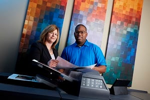 Two employees standing by a multi-function printer reviewing a document together