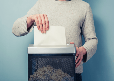 Image of a person's torso standing behind a document shredder. The person is shredding a document.