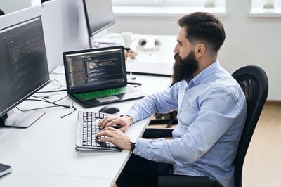 man sitting at his desk looking at code on his computer