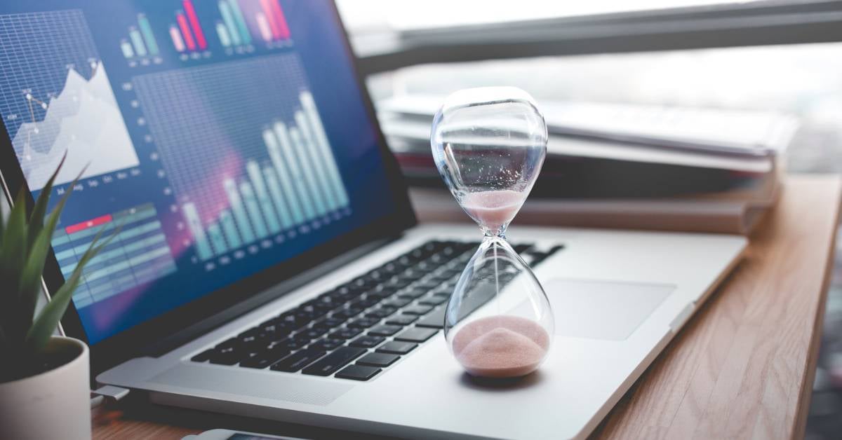 An hourglass rests on an open laptop where real-time analytics are displayed on the screen.