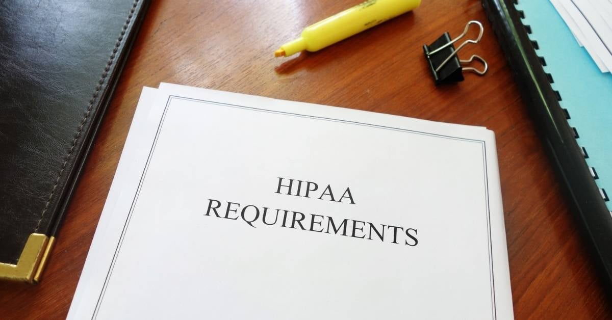 A binder with HIPAA requirements on a desk with yellow highlighter.