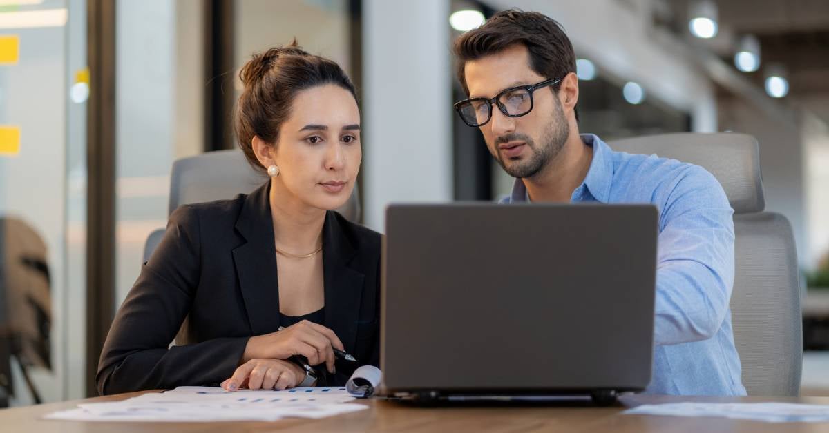 An IT leader meets with an executive to go over data on a laptop.