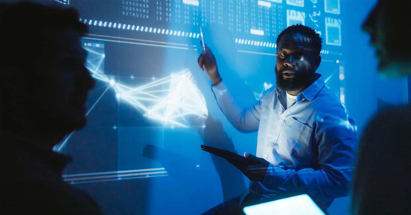 A man presents data to colleagues in front of a digitized screen. 