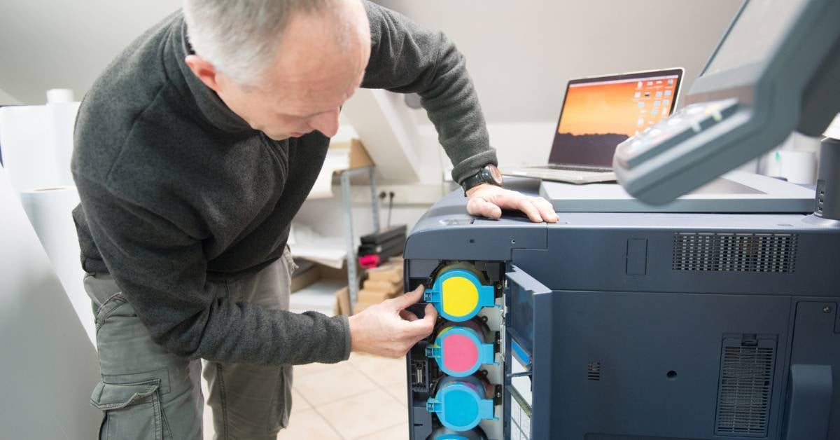 A copier technician loads toner into a printing device.