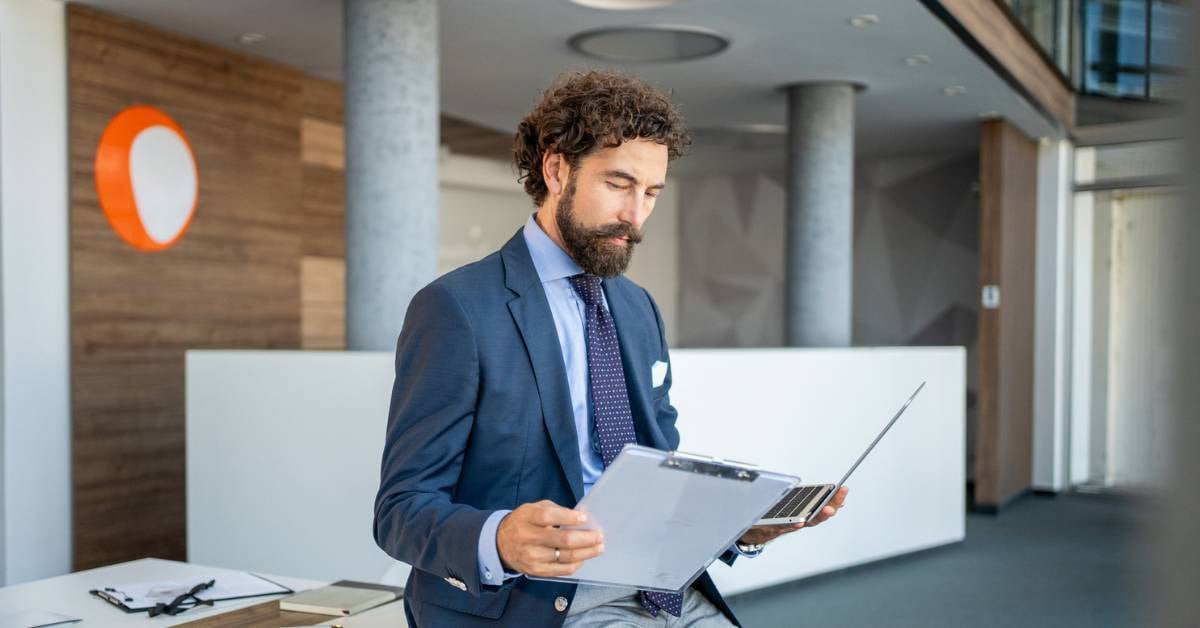 A male employee at a professional services organization holding a tablet and a laptop.