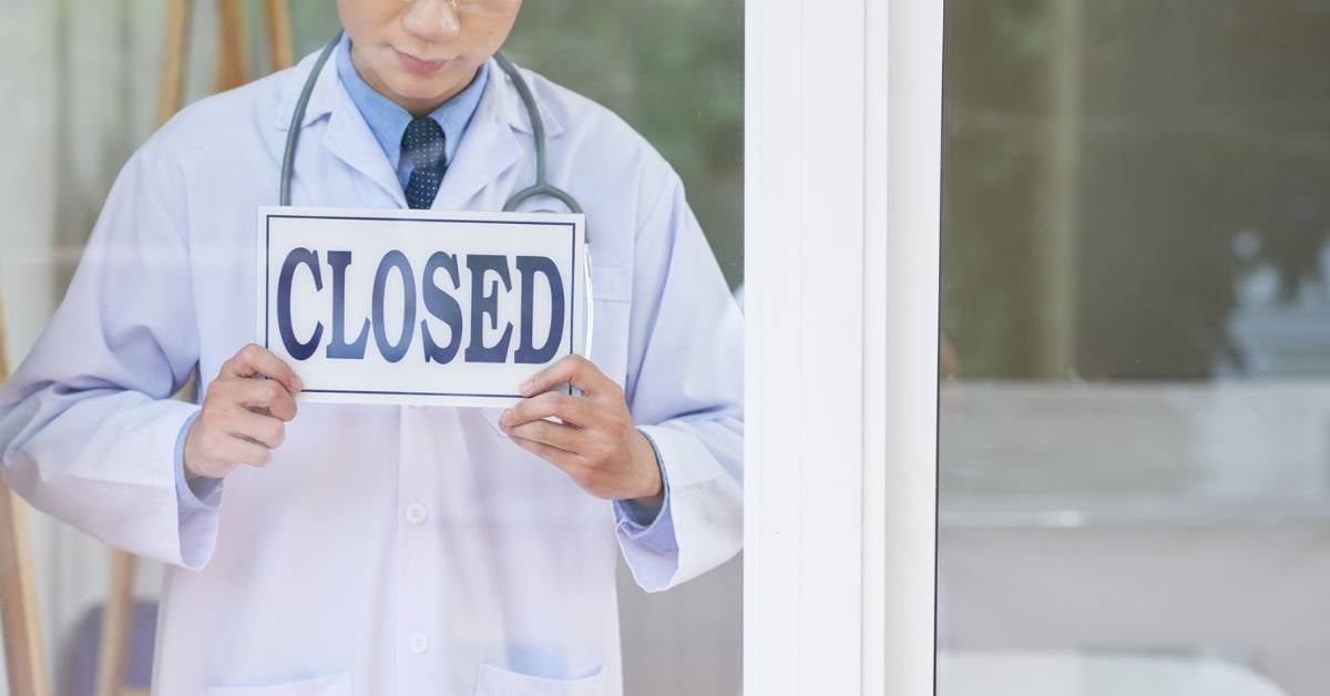 A close-up of a doctor holding up a closed sign.