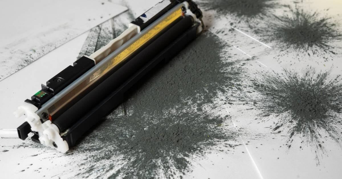 A toner cartridge with powder leaking onto paper.