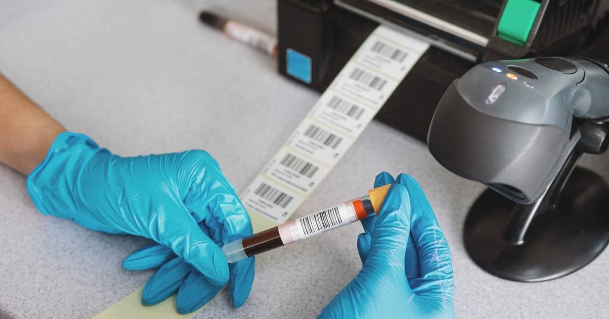 A hospital worker wearing protective gloves checks labels coming out of a thermal printer