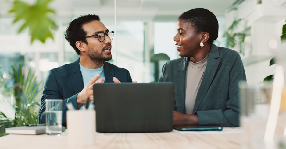 Two business leaders in a meeting facing an open laptop. 