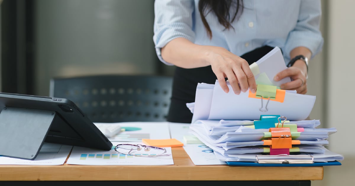 A closeup on a worker sorting through a pile of papers on a desk.