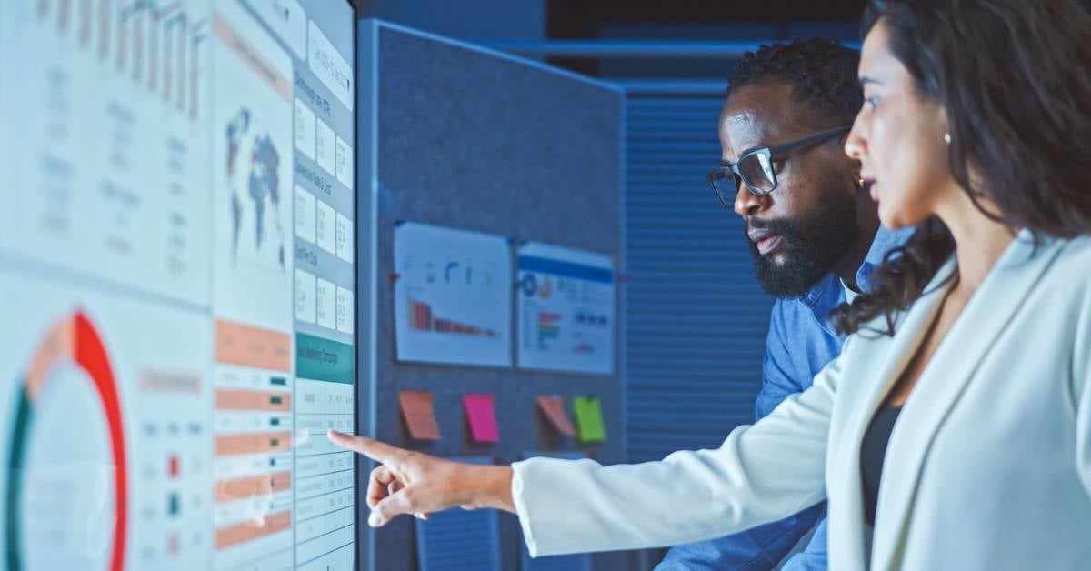 Two coworkers talk through the ROI of a particular solution on a touchscreen.