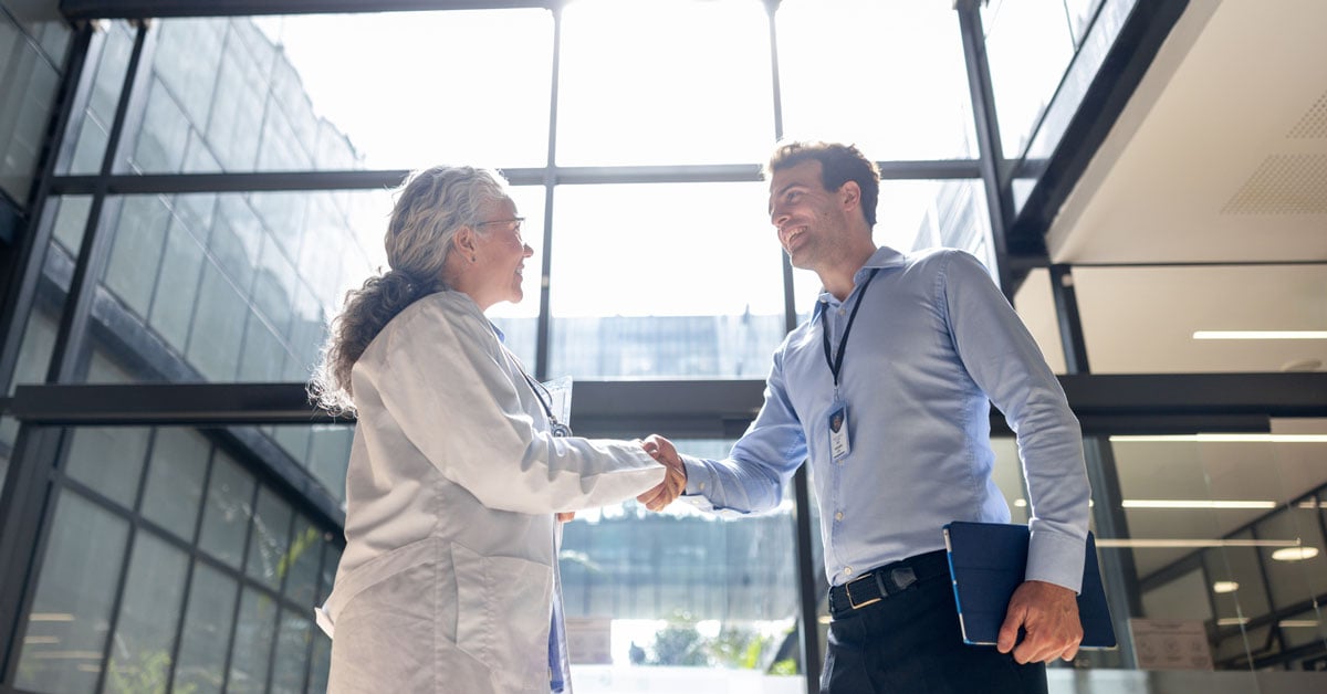 A healthcare professional and a managed print services provider shake hands in a healthcare facility lobby.