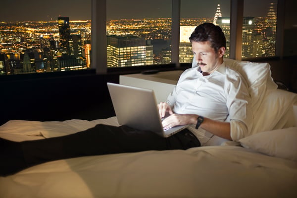 Employee working remotely in a hotel room with a laptop at night.