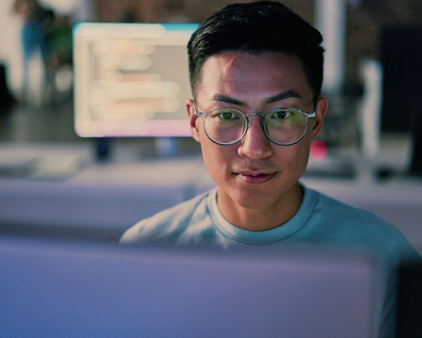 Man wearing glasses looking at a computer screen at his desk.