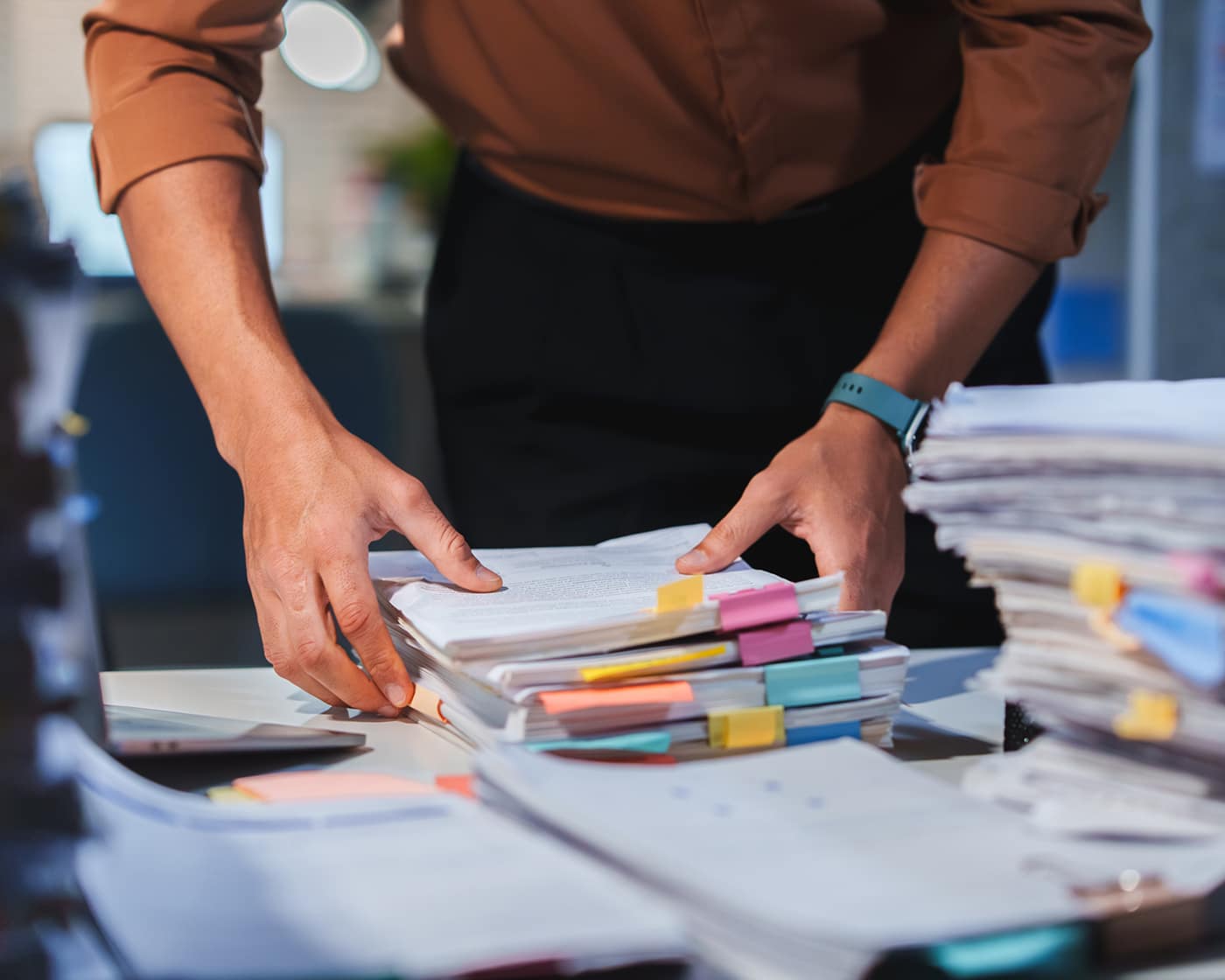 person-reviewing-stacked-documents-with-colorful-sticky-tabs-at-desk