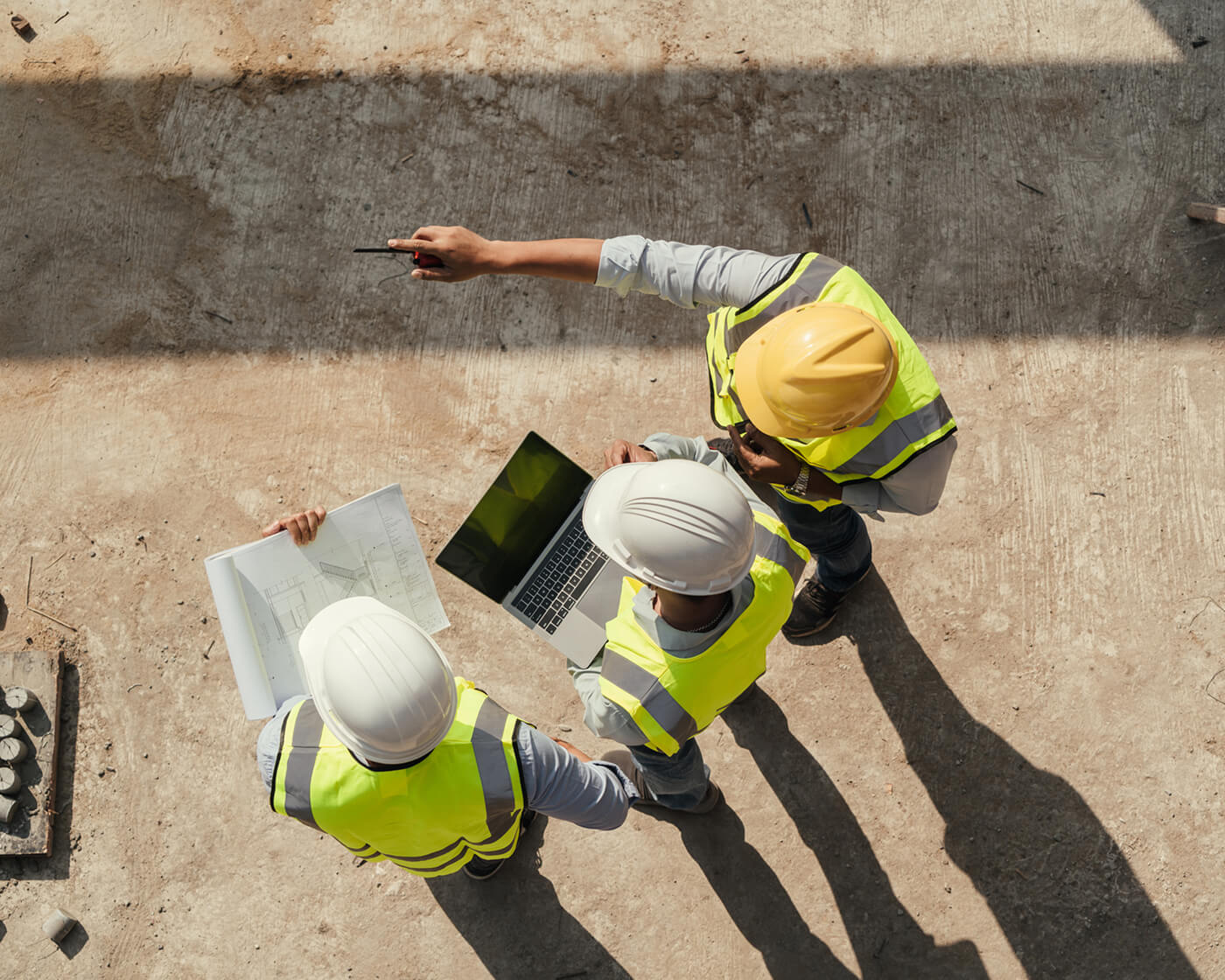 An overhead view of three construction workers looking over a blueprint.