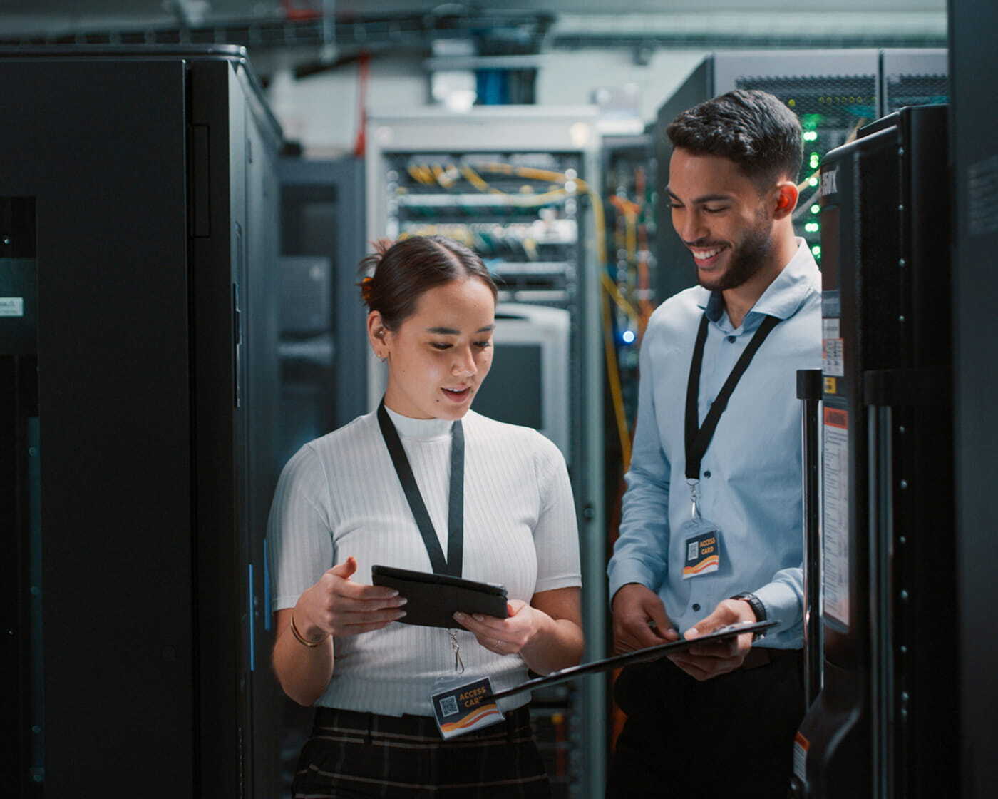 Two smiling coworkers standing together in a server room.