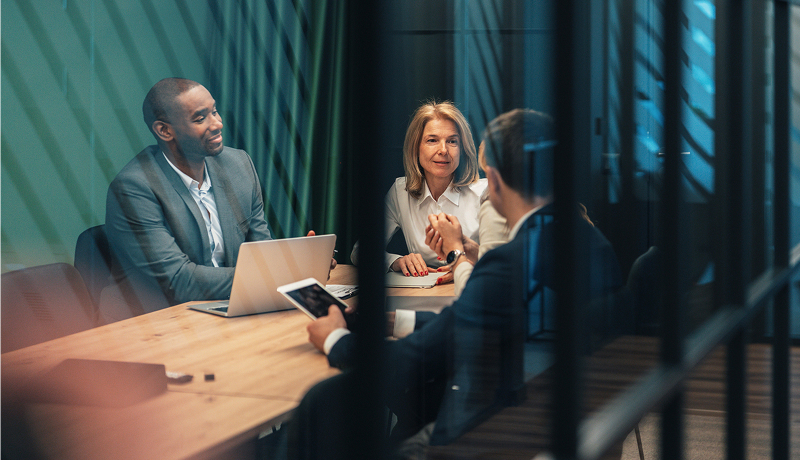 Three business professionals having a discussion together in a glass-walled conference room