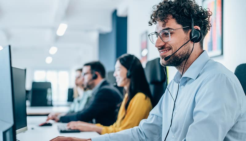 man-wearing-headset-smiling-at-computer-in-office-call-center