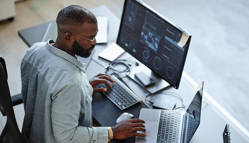 man-working-at-desk-with-multiple-computer-monitors-and-laptops