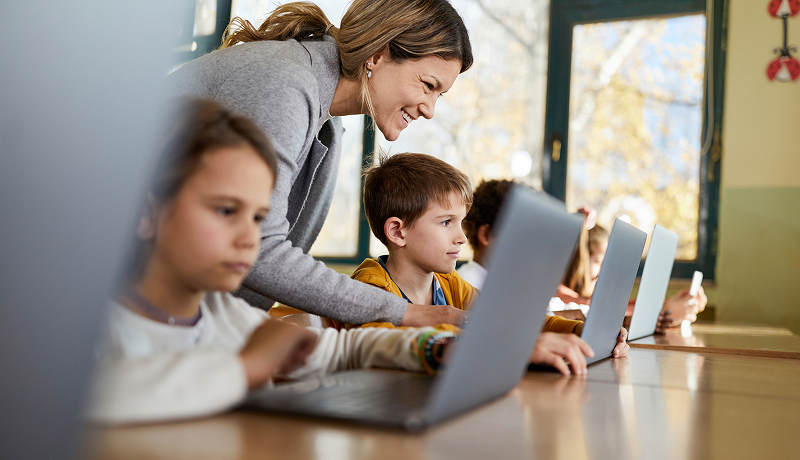 A teacher helping students on laptops.