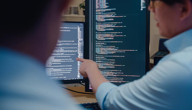 Two developers reviewing code together on dual monitors.