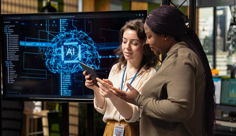 Two coworkers discussing an AI neural network visualization on a display screen.