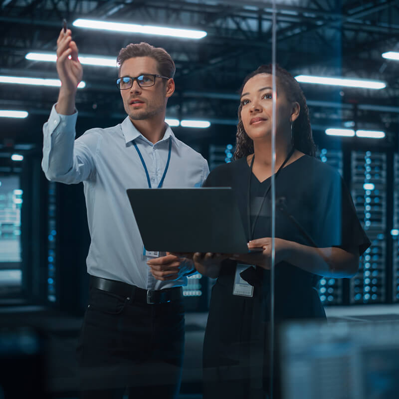 Colleagues discussing data on a laptop in a server room.