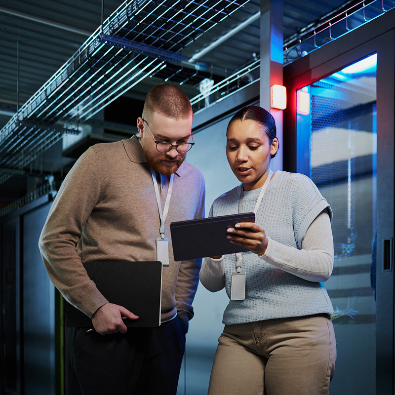 IT team members reviewing data on a tablet in a server room.