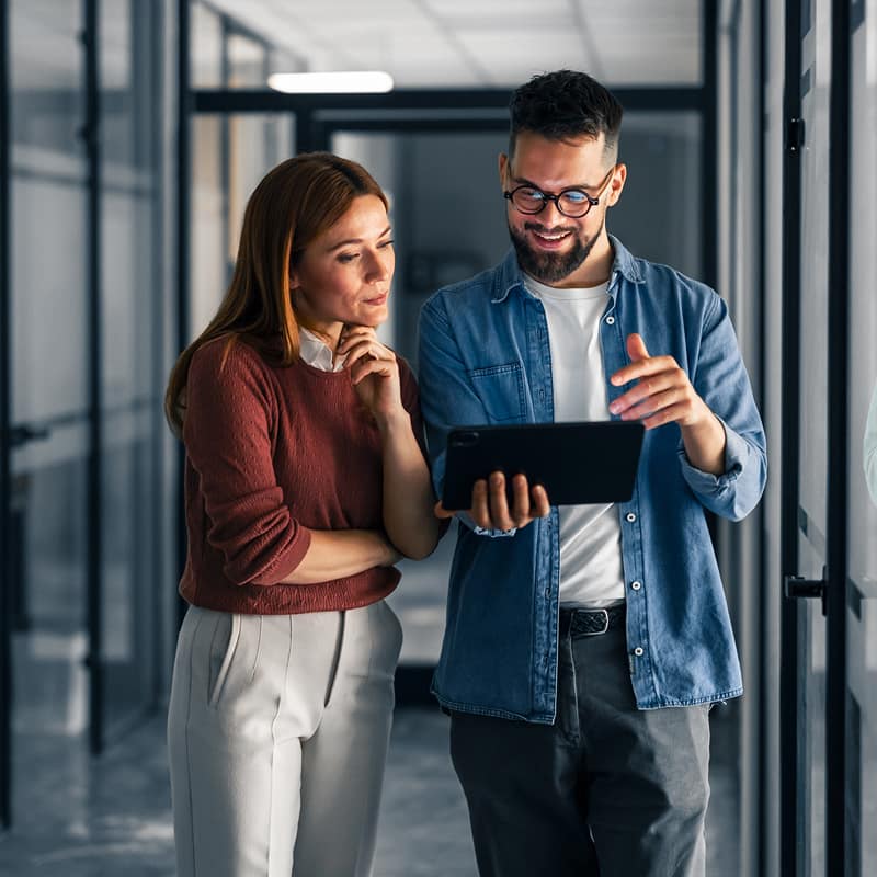 man-and-woman-reviewing-tablet-together-in-modern-office-hallway