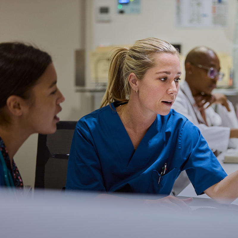 Two nurses reviewing patient documents together at a computer.
