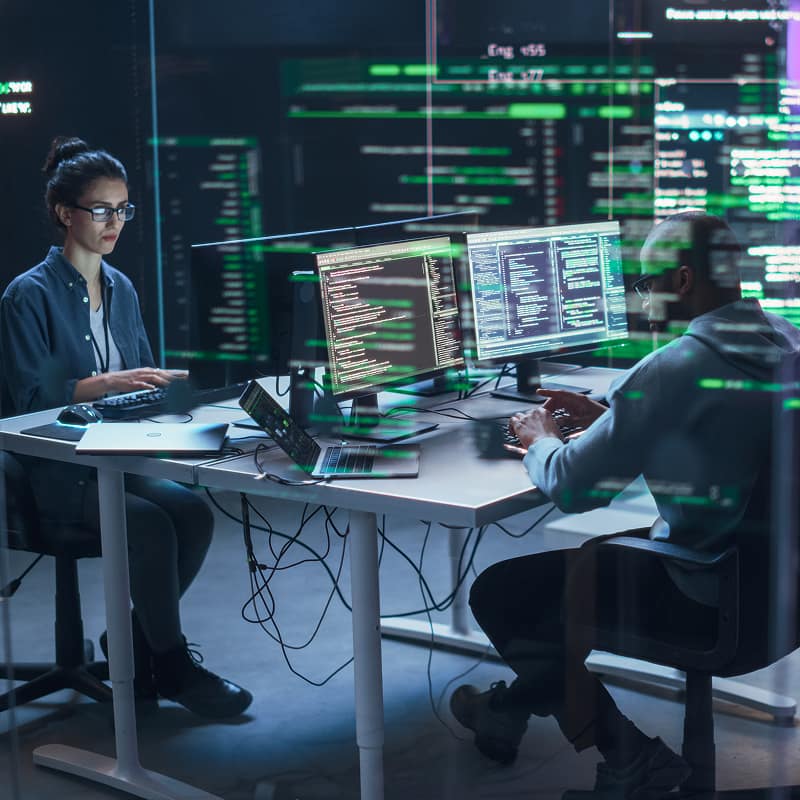 two-software-engineers-working-at-desk-with-multiple-monitors-displaying-code