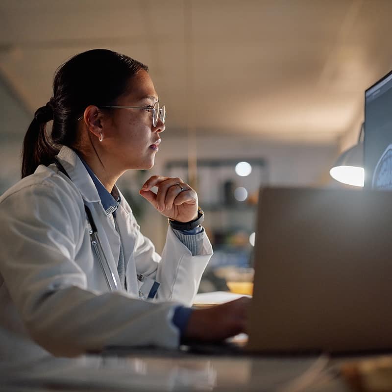 woman-in-lab-coat-wearing-glasses-thinking-while-looking-at-computer-screen