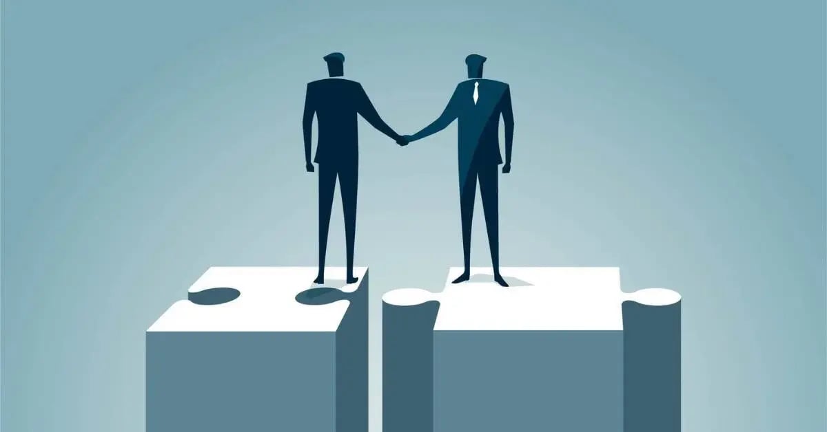 Two business leaders shaking hands while standing on puzzle pieces that fit together.