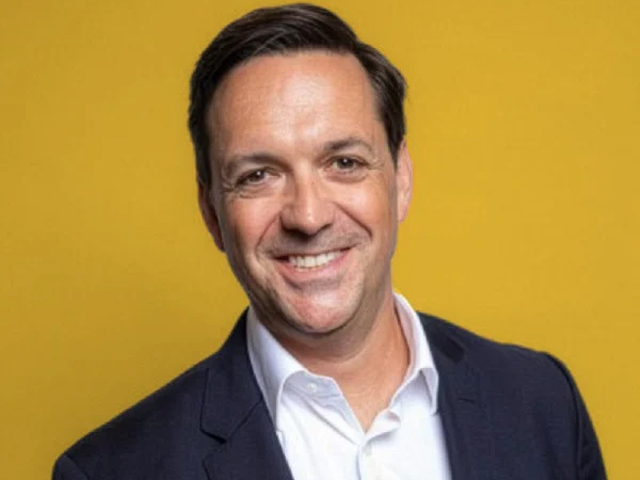 Portrait of Brian Wyatt smiling against a yellow background.