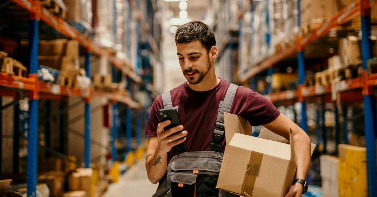 Manufacturer-with-cell-phone-holding-a-box-on-production-floor