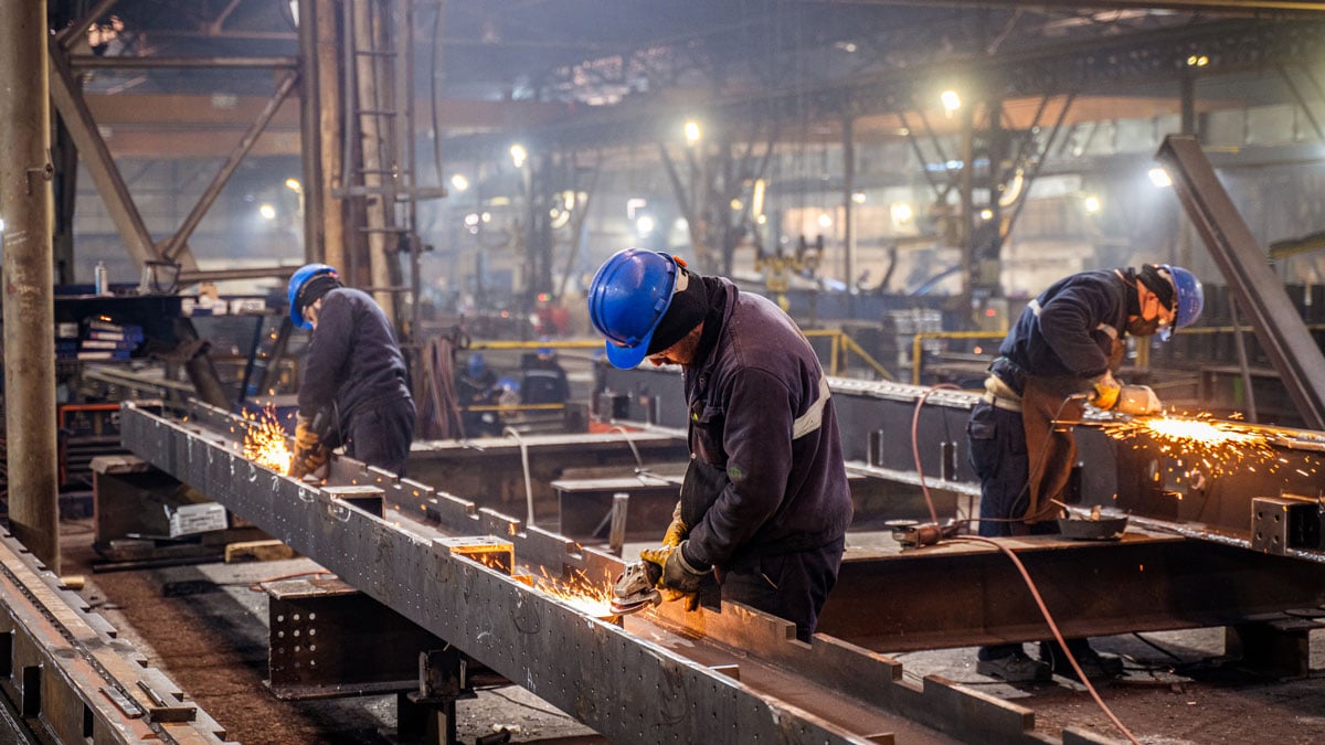 Metal workers using grinders on a factory floor.