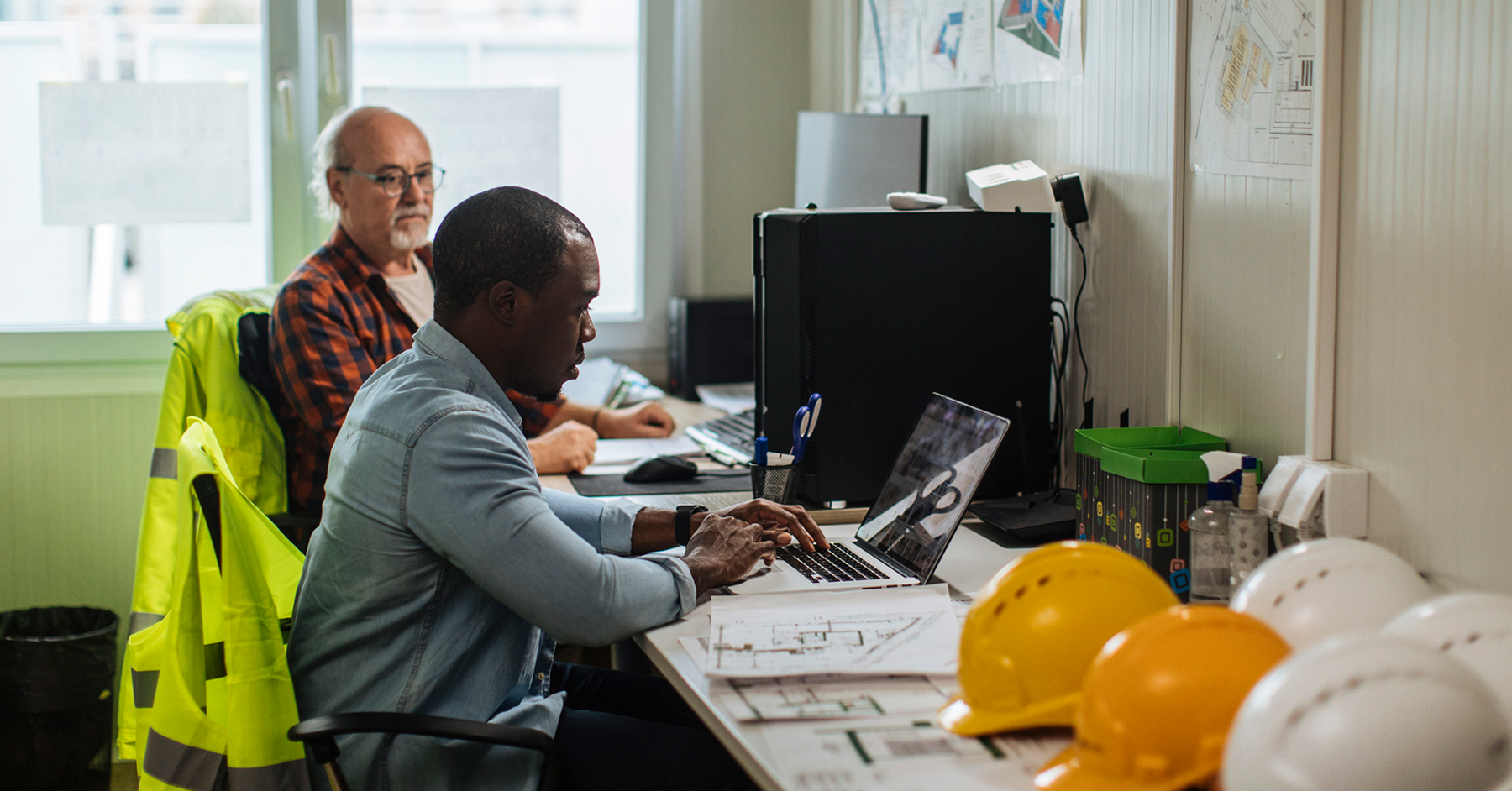two-construction-workers-in-trailer-with-computer-and-blueprints